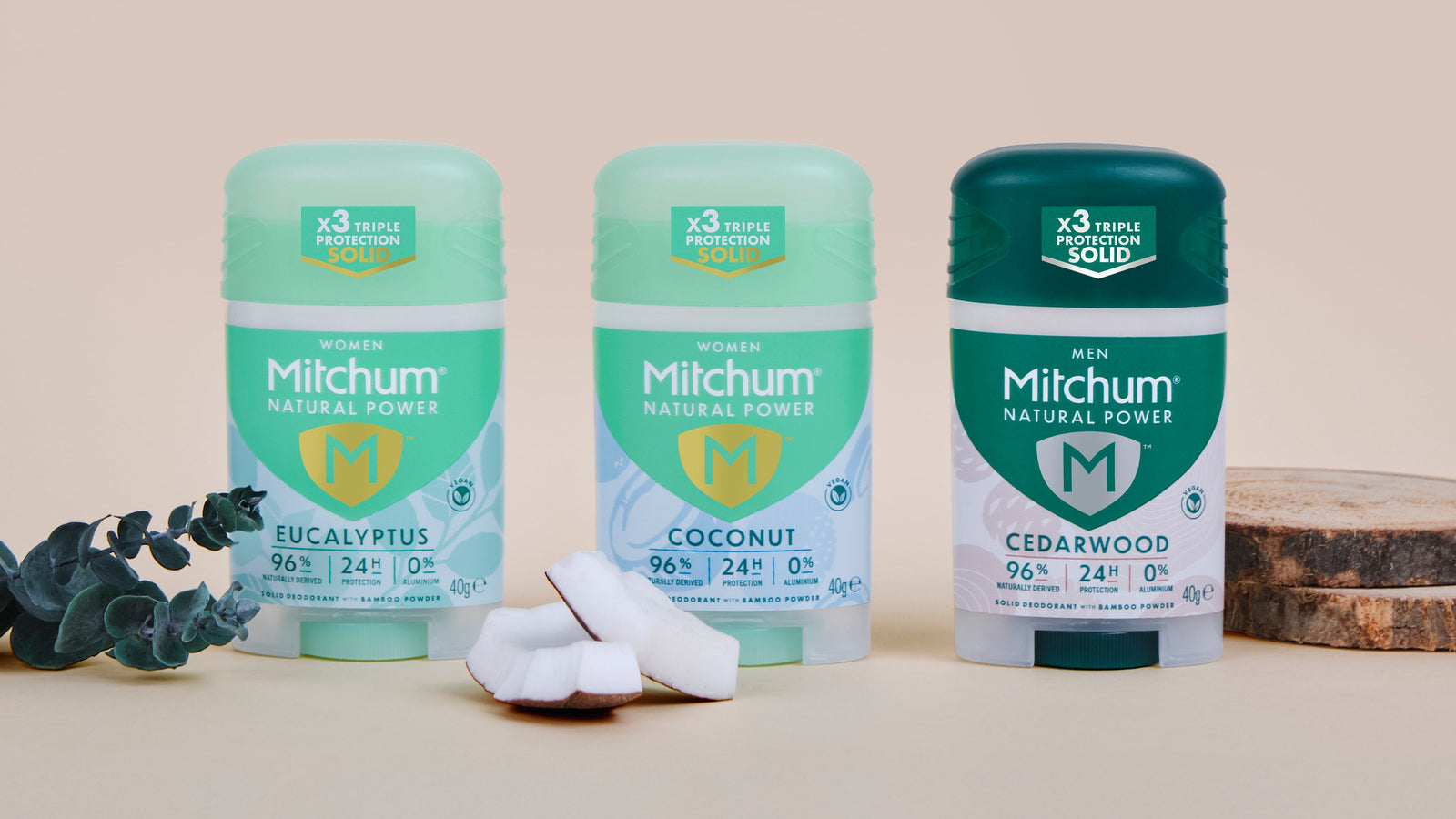 Three Mitchum solid deodorant containers on a neutral background with eucalyptus leaves.